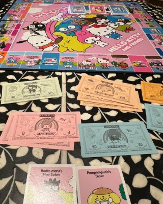 A Hello Kitty and Friends Monopoly board with Sanrio banknotes and property cards spread out beside it.