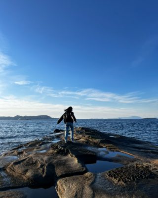 A figure silhouetted on sandstone tide pools at the shore of Gabriola Island under a deep blue sky.